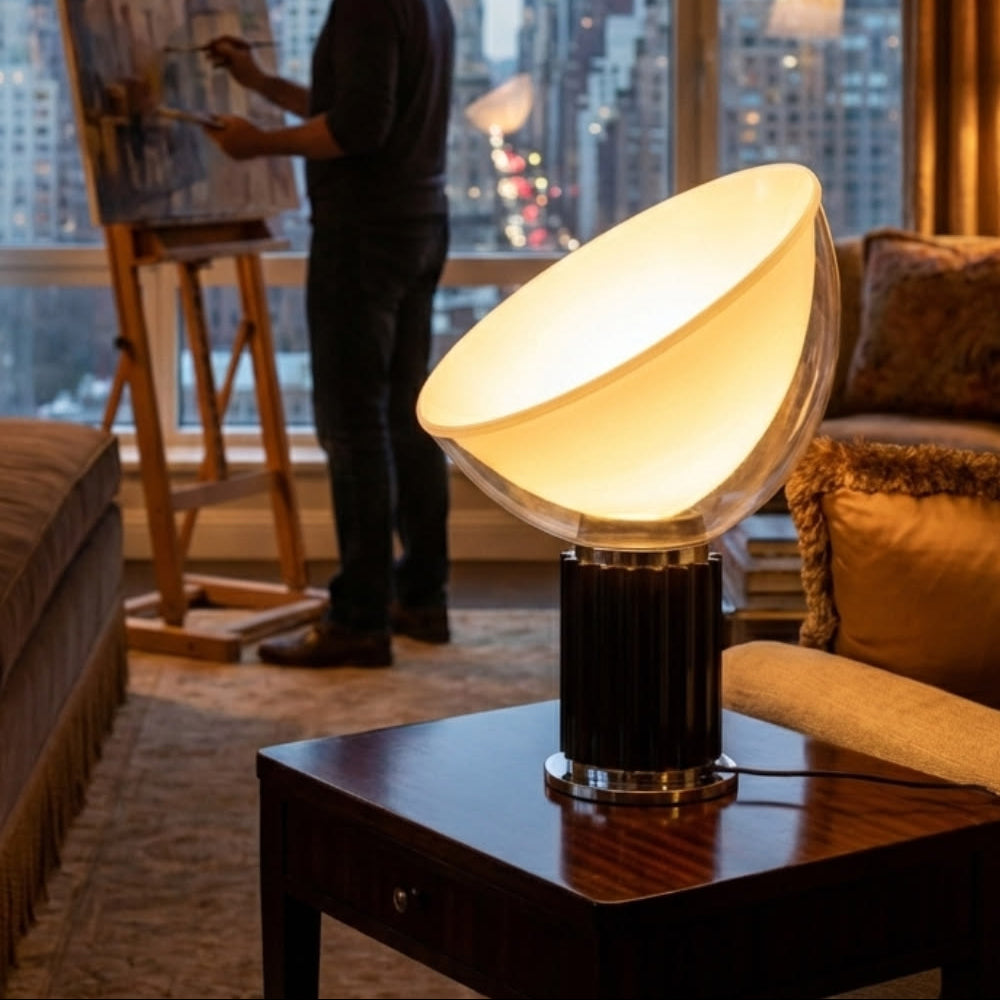 Man painting a cityscape with a large lamp on a table in the foreground.